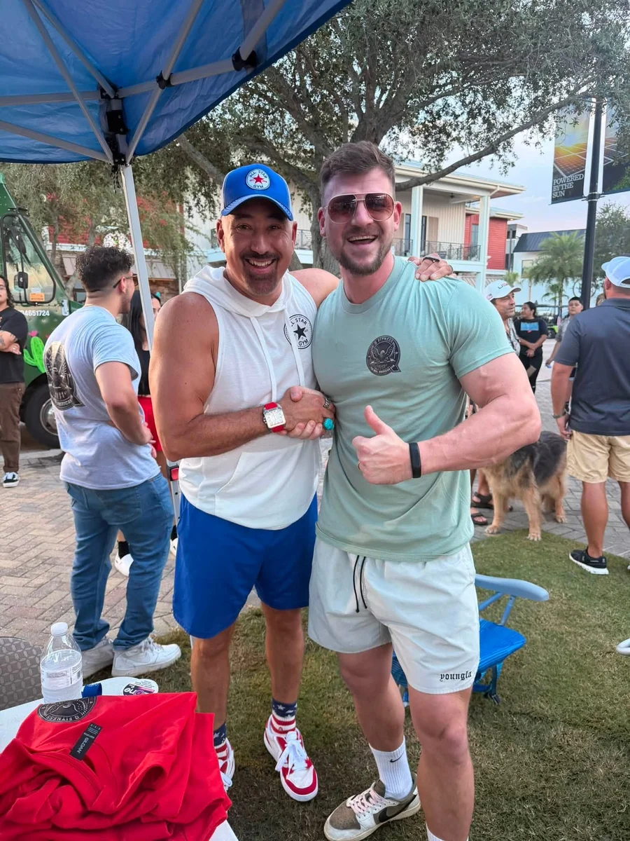 A Q Fitness team member shaking hands with a visitor from All Star Gym under the Q Fitness
                    tent at Food Truck Night, a food truck and the Babcock Ranch solar banner in the background.