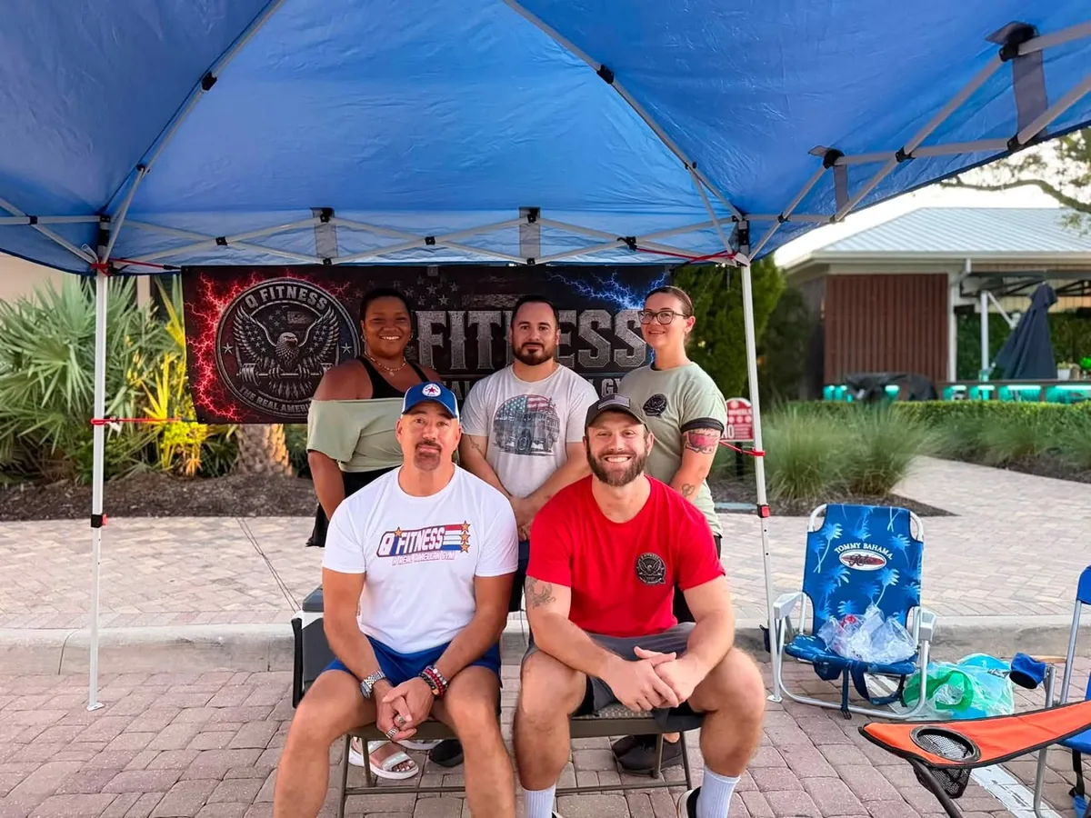 The Q Fitness team standing together under a tent in front of a Q Fitness banner at a community event.